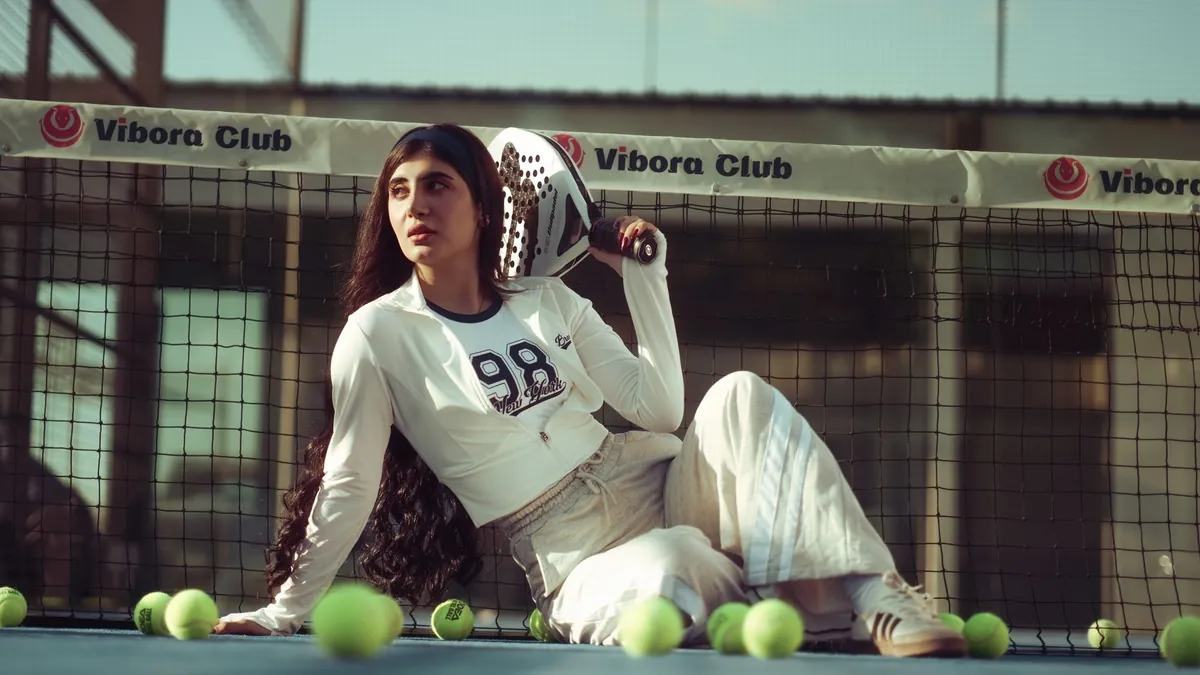 Young woman tennis player sitting on court, surrounded by tennis balls, in vibora club setting.